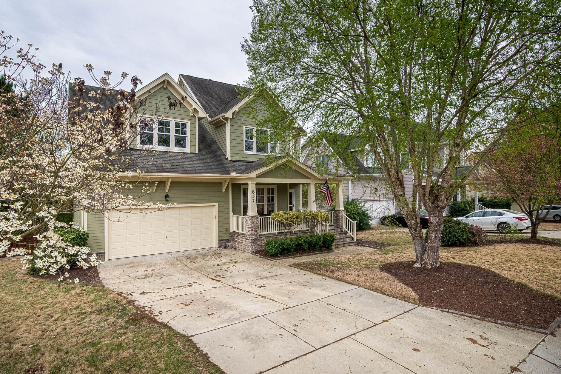 A picturesque suburban home with a lush front yard, driveway, and trees.