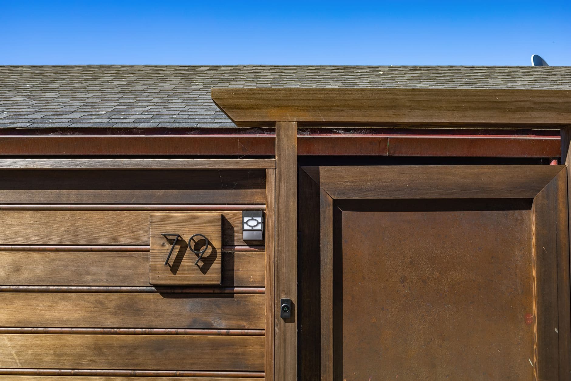 Stylish wooden door with house number 79 under clear blue sky.