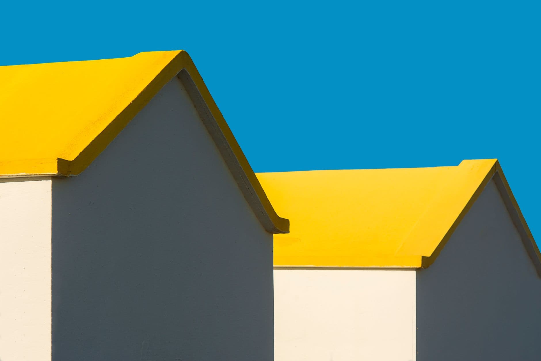 Bright yellow roofs contrasted by a vibrant blue sky create a striking minimalist architectural image.