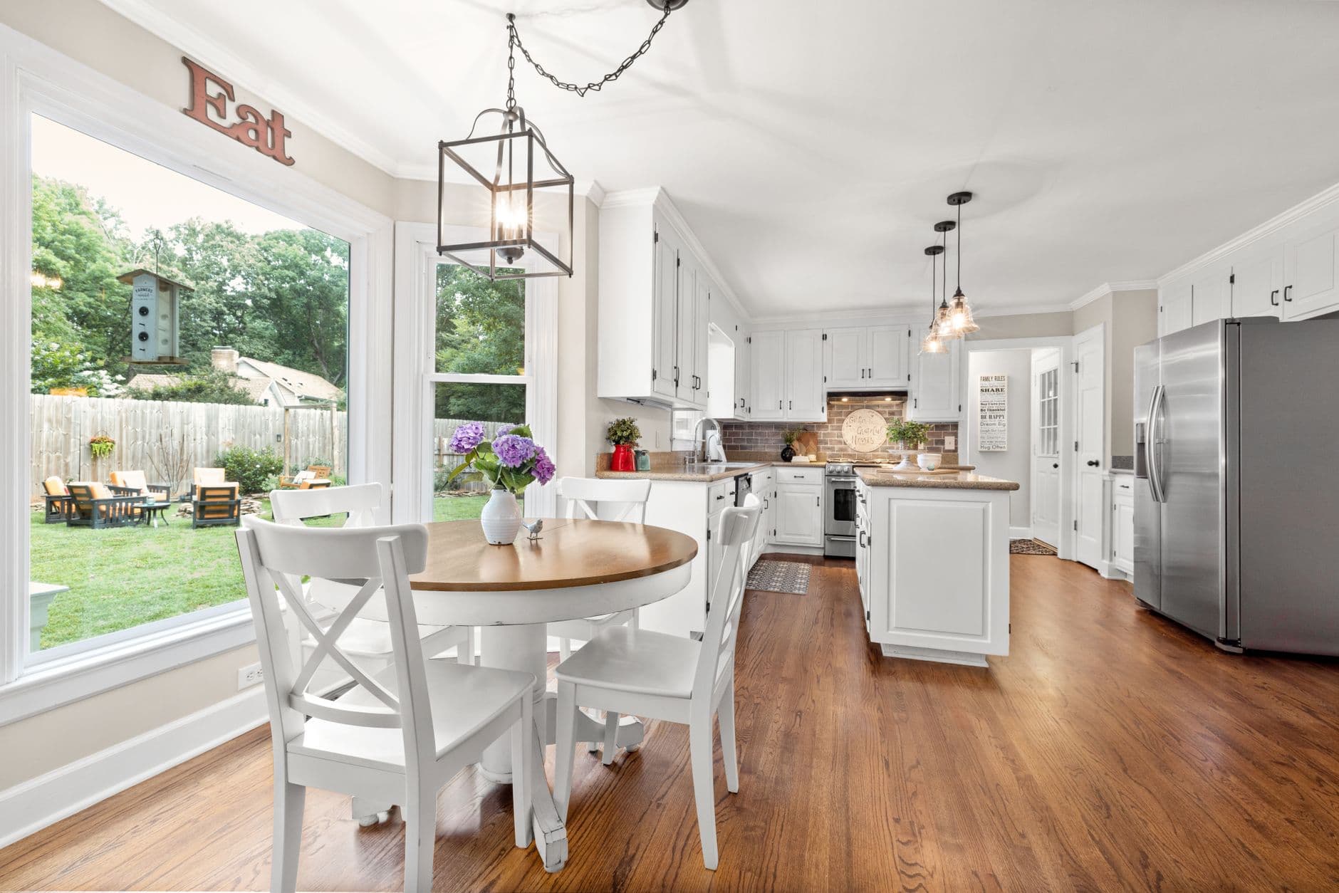 Modern kitchen with white cabinets and dining area with outdoor view.