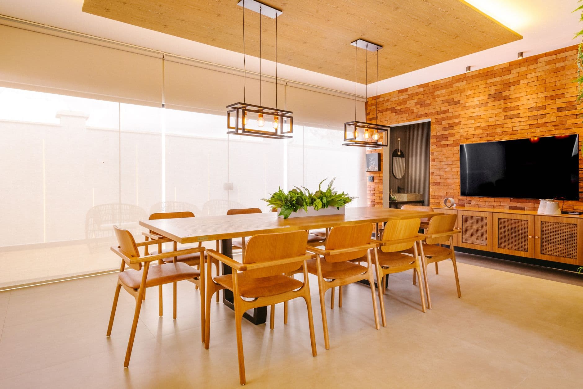 Spacious dining area featuring wooden furniture, brick wall, and indoor plants under modern lighting.