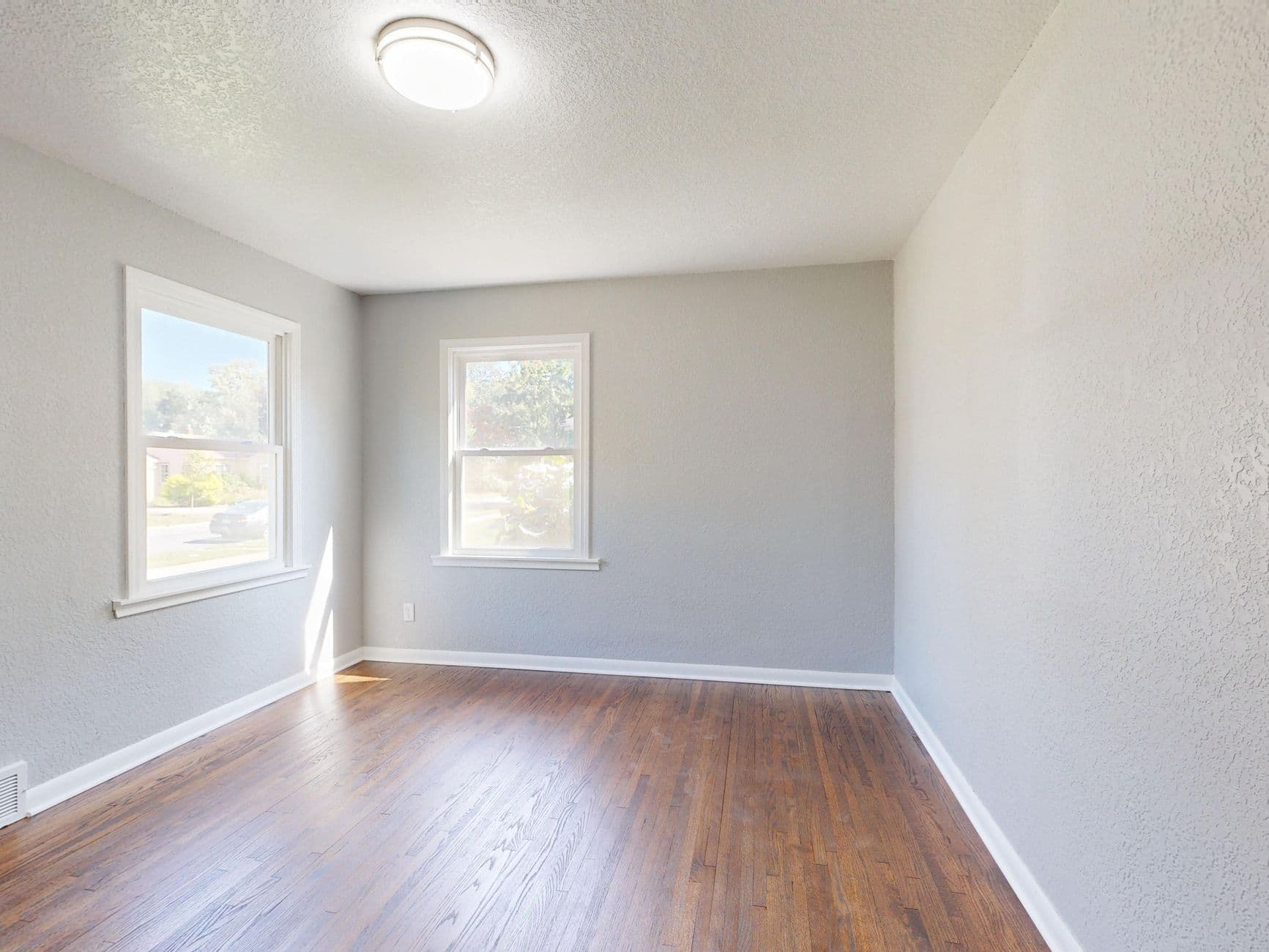 Well-lit empty room featuring hardwood floors and large windows.