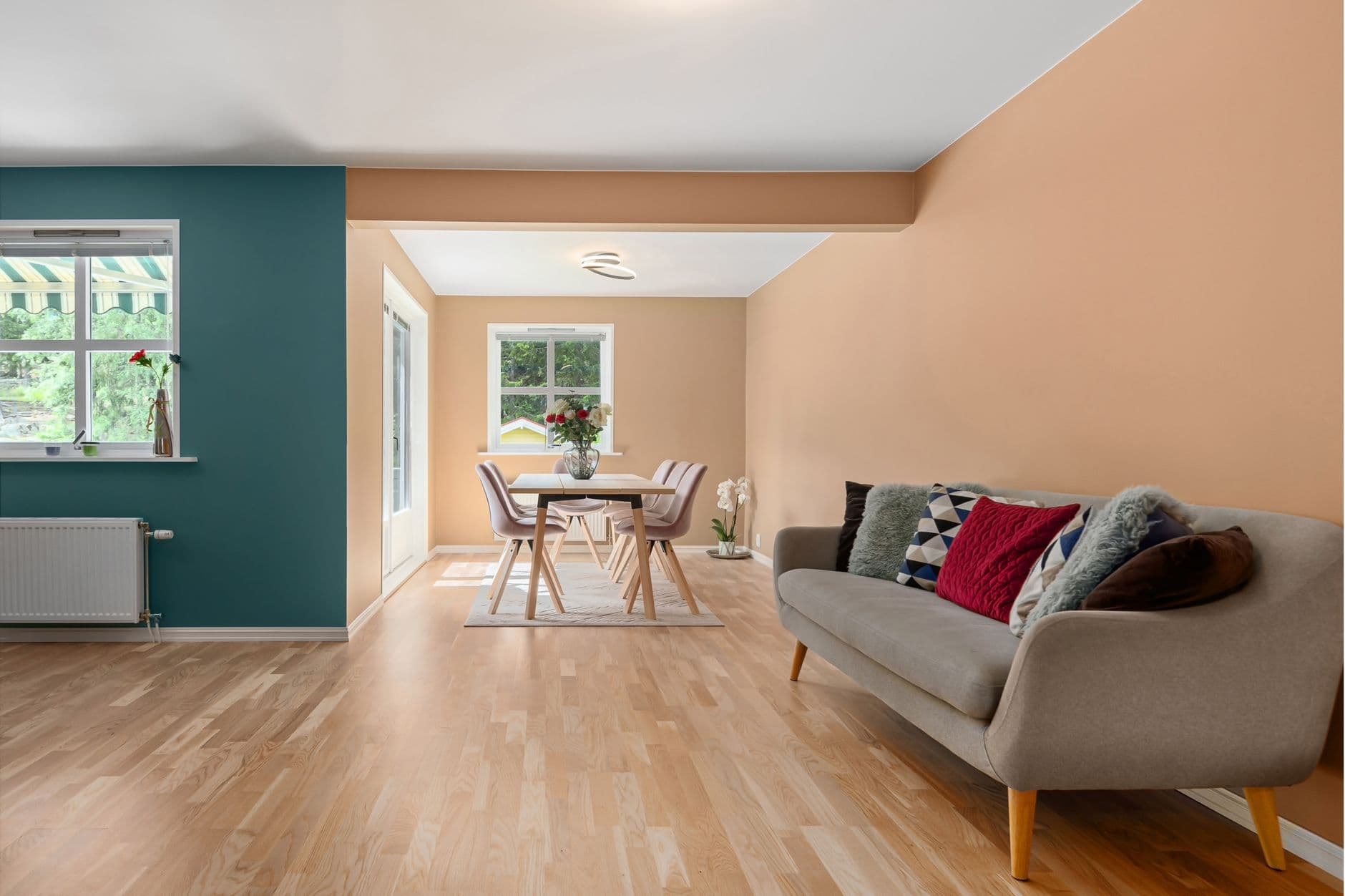 A stylish living room showcasing minimalist design with a cozy sofa, vibrant pillows, and a spacious dining area.