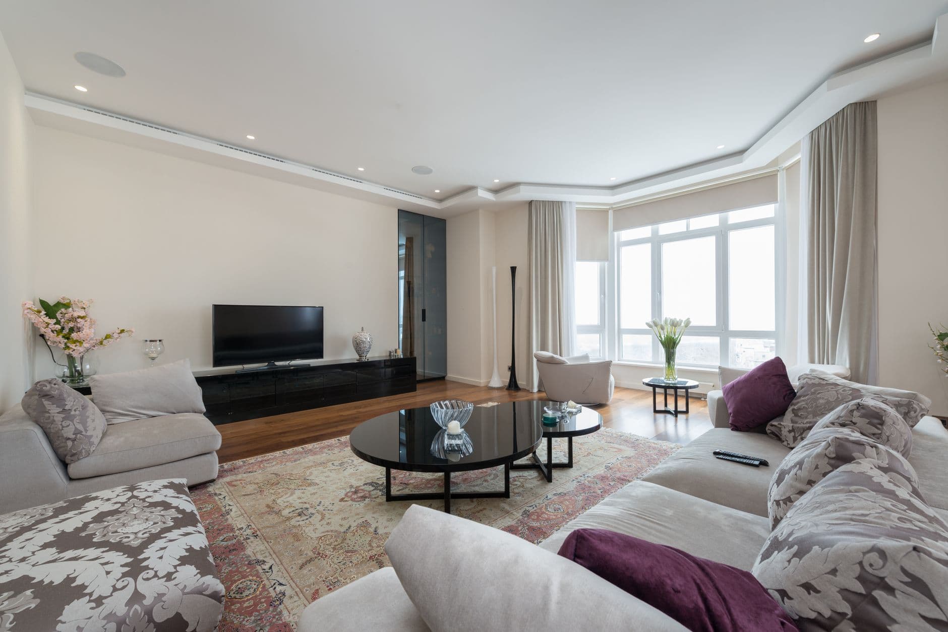 Elegant interior of spacious living room with soft sofas and armchairs placed near coffee tables and TV set in modern apartment
